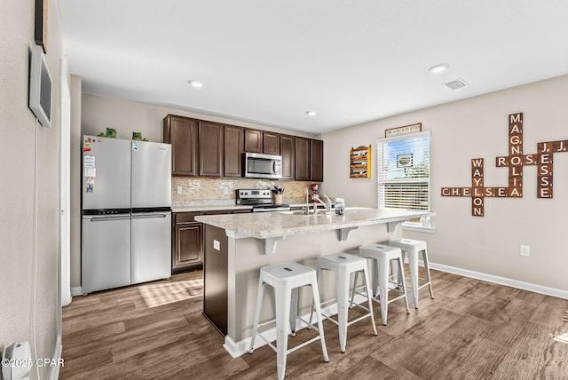 kitchen featuring wood finished floors, visible vents, stainless steel appliances, dark brown cabinetry, and tasteful backsplash