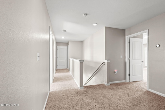 corridor with visible vents, an upstairs landing, baseboards, and carpet floors