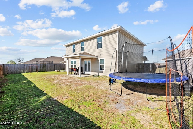 back of house featuring a patio area, a trampoline, a fenced backyard, and a yard