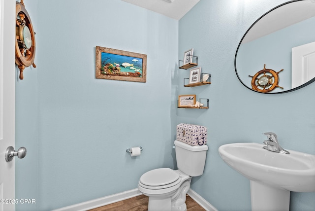 half bath with baseboards, toilet, and wood finished floors