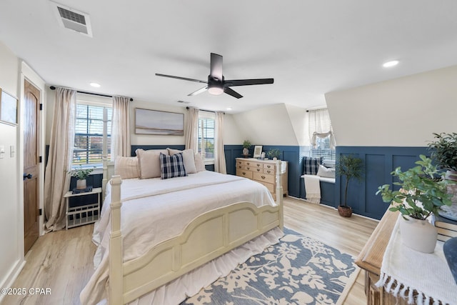 bedroom featuring light wood-style flooring, a ceiling fan, visible vents, and wainscoting