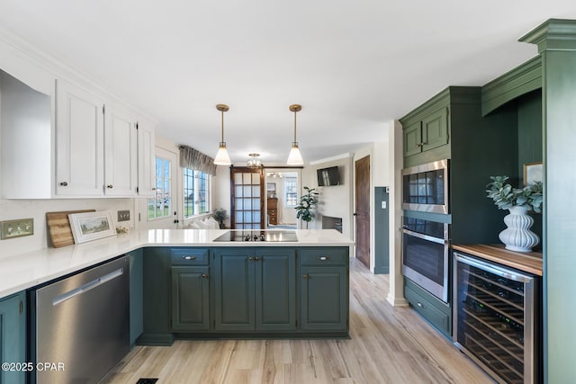 kitchen featuring beverage cooler, a peninsula, light countertops, appliances with stainless steel finishes, and white cabinetry