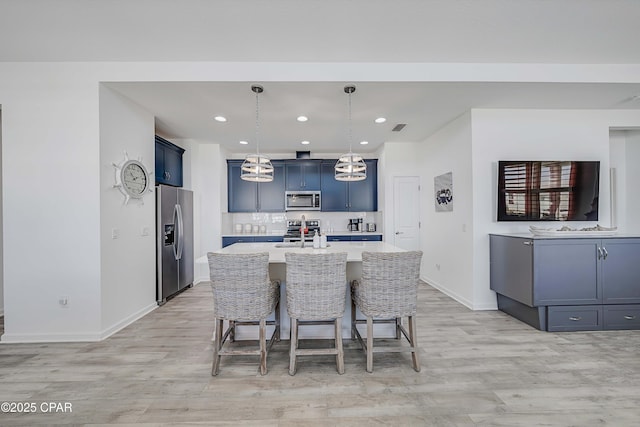 kitchen featuring an island with sink, stainless steel appliances, light countertops, light wood-style floors, and a kitchen breakfast bar