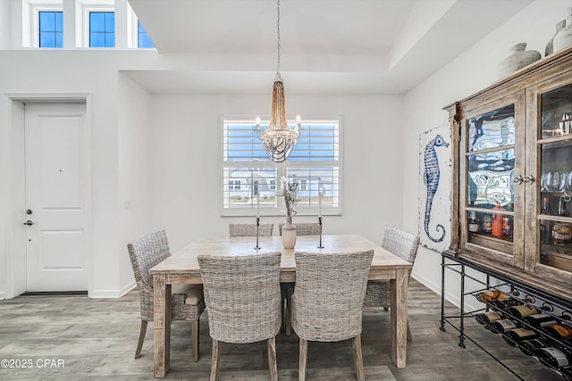 dining room featuring baseboards, a raised ceiling, an inviting chandelier, and wood finished floors