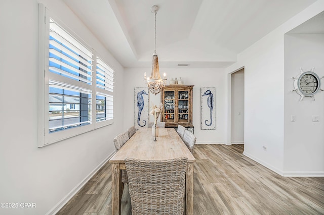 dining space featuring a notable chandelier, baseboards, a tray ceiling, and light wood-style floors