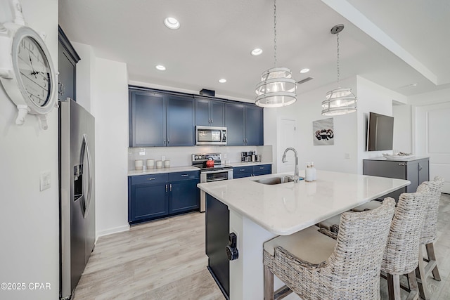 kitchen with light wood finished floors, blue cabinetry, a breakfast bar area, appliances with stainless steel finishes, and a sink