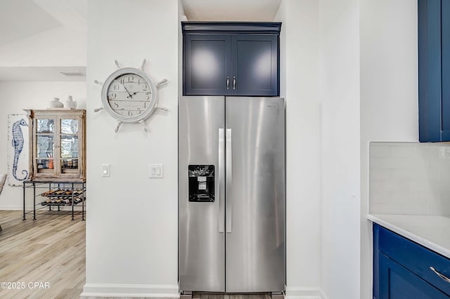 kitchen with blue cabinets, light wood-type flooring, baseboards, and stainless steel refrigerator with ice dispenser