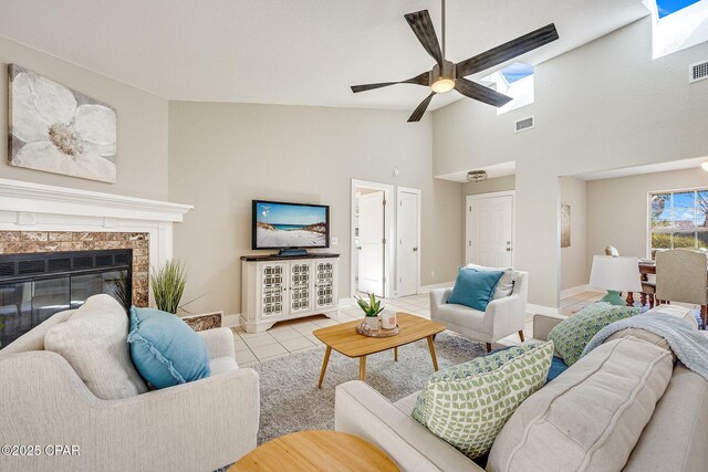 tiled living room with visible vents, baseboards, a glass covered fireplace, and a ceiling fan