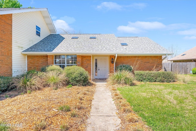 view of front of property featuring a front yard, fence, brick siding, and roof with shingles