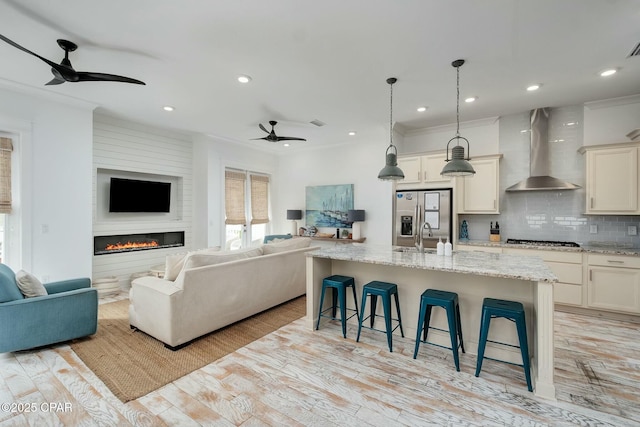 living area with ceiling fan, light wood-type flooring, recessed lighting, ornamental molding, and a fireplace