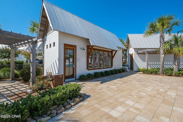 view of front facade featuring a patio area, stucco siding, metal roof, and a pergola
