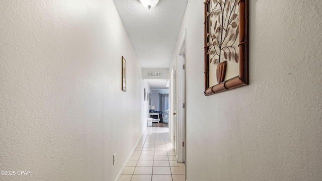 corridor with light tile patterned flooring, a textured ceiling, baseboards, and a textured wall