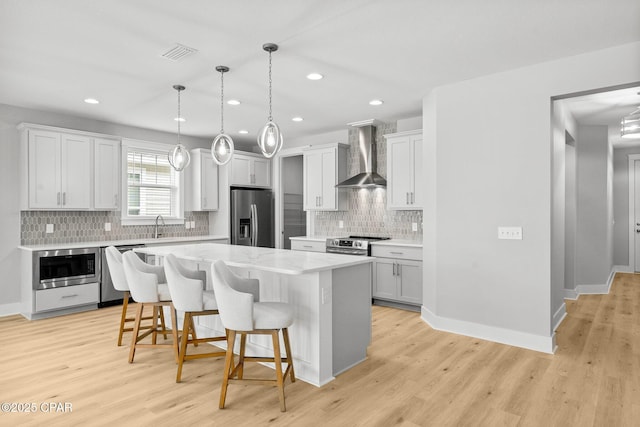 kitchen featuring visible vents, a kitchen island, stainless steel appliances, wall chimney exhaust hood, and light countertops