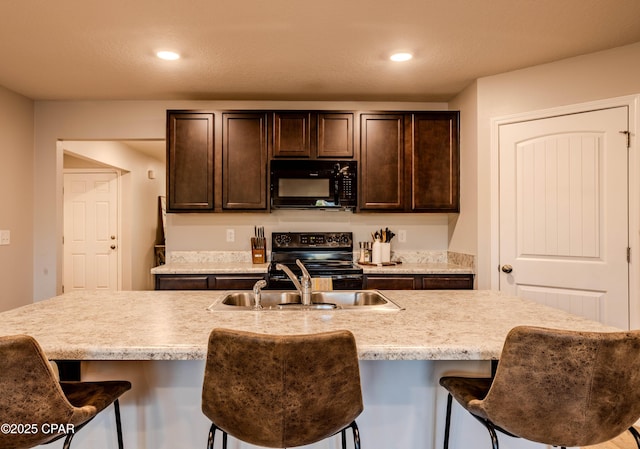 kitchen featuring a kitchen bar, black appliances, dark brown cabinets, and recessed lighting