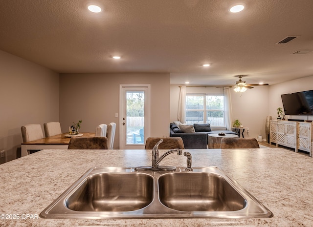 kitchen featuring visible vents, recessed lighting, a sink, a textured ceiling, and open floor plan