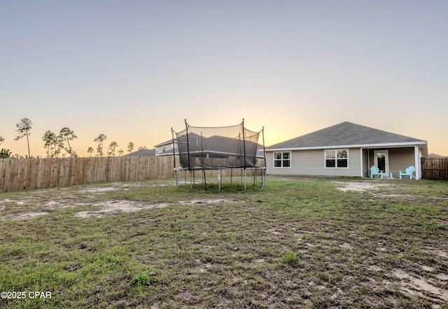 yard at dusk featuring a trampoline and a fenced backyard