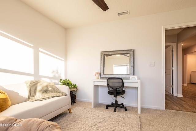 carpeted office space featuring baseboards, visible vents, and ceiling fan