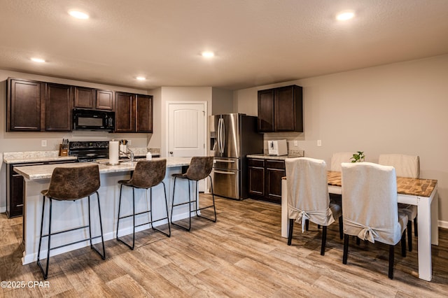 kitchen with dark brown cabinets, light wood-type flooring, a kitchen bar, and black appliances