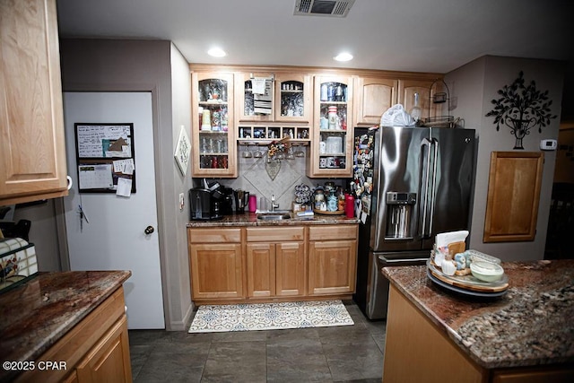 kitchen with visible vents, glass insert cabinets, dark stone countertops, stainless steel refrigerator with ice dispenser, and a sink