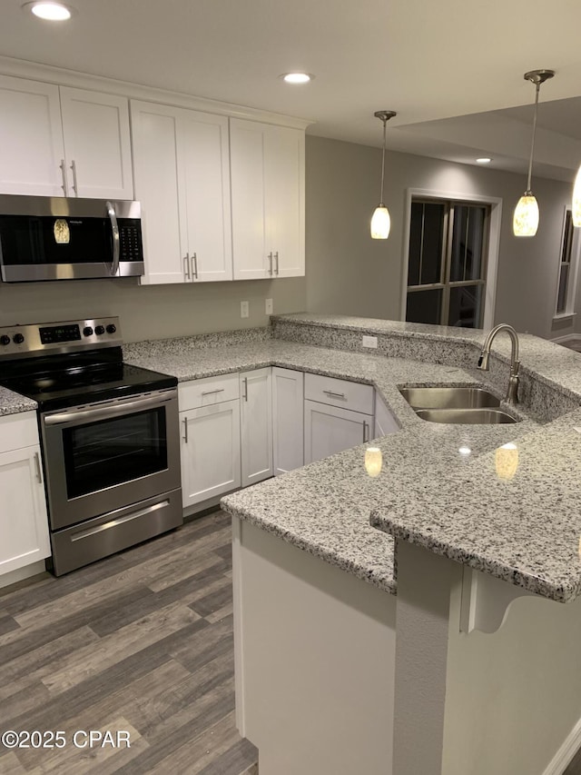 kitchen with dark wood-style floors, a sink, white cabinets, appliances with stainless steel finishes, and decorative light fixtures