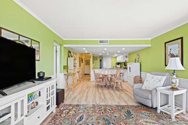 living room featuring light wood-style floors, crown molding, visible vents, and a wainscoted wall