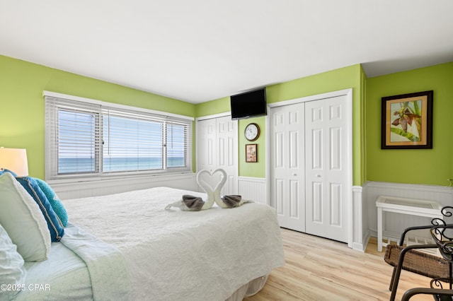 bedroom featuring light wood-type flooring, multiple closets, and wainscoting