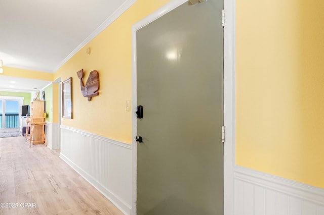 hallway with ornamental molding, light wood-style floors, and wainscoting