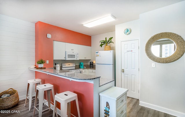 kitchen featuring a kitchen breakfast bar, wood finished floors, white appliances, a peninsula, and white cabinets