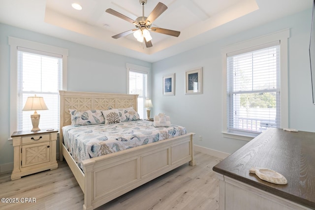 bedroom with light wood-style flooring, baseboards, a tray ceiling, and ceiling fan