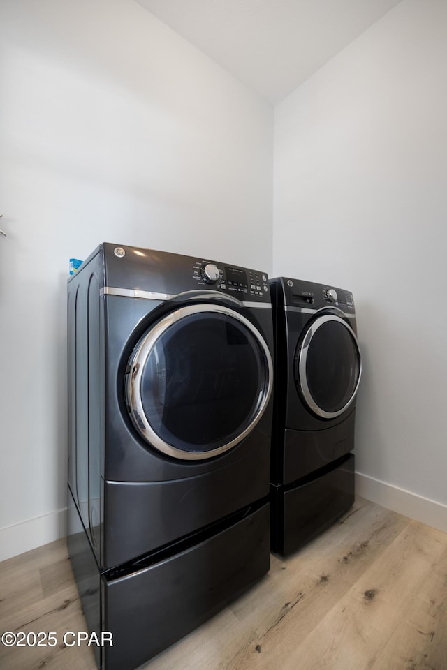 washroom featuring washer and dryer, laundry area, wood finished floors, and baseboards