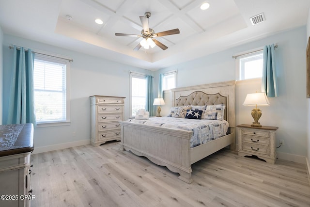 bedroom with light wood-style floors, baseboards, visible vents, and a tray ceiling