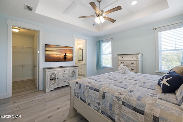 bedroom with a walk in closet, a tray ceiling, light wood-style flooring, and visible vents