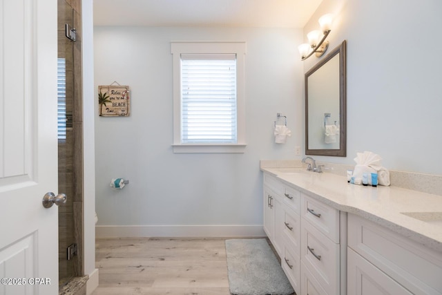 full bathroom featuring a shower stall, baseboards, double vanity, wood finished floors, and a sink