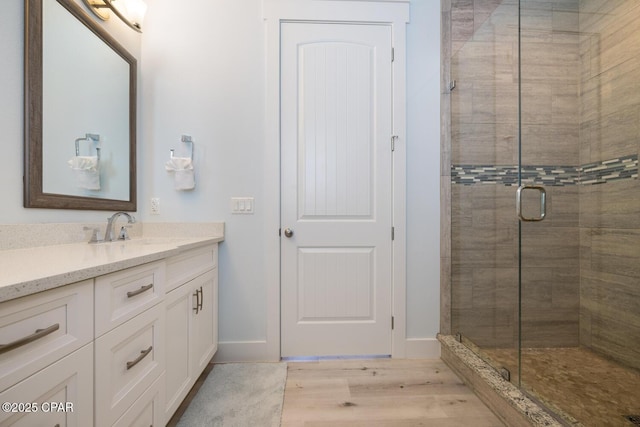 bathroom with vanity, wood finished floors, baseboards, and a stall shower