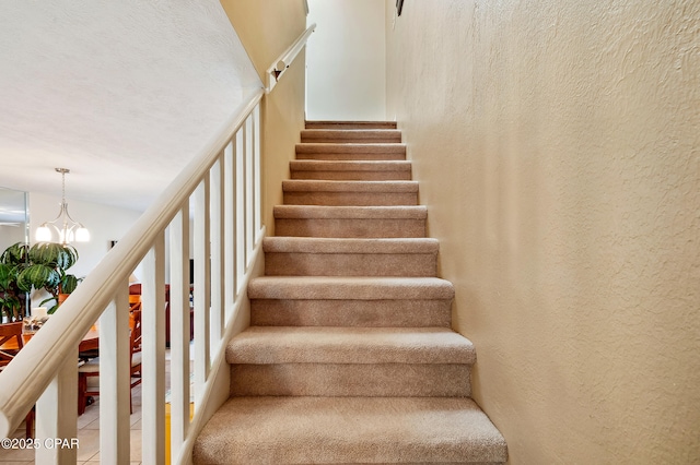 stairs featuring a notable chandelier and a textured wall