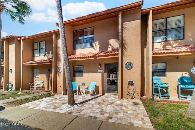 back of house featuring stucco siding, a tiled roof, and a patio