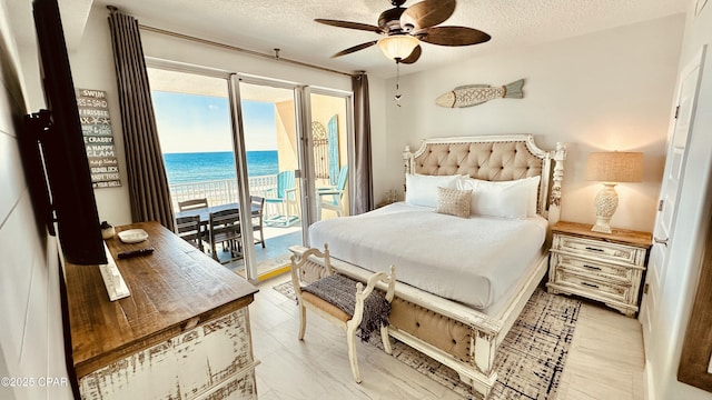 bedroom with a water view, a ceiling fan, access to outside, a textured ceiling, and a view of the beach