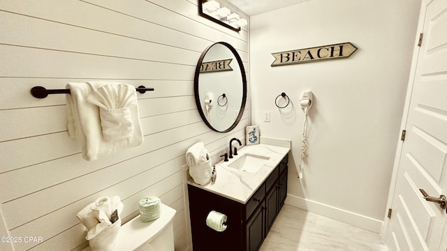 half bath with marble finish floor, a textured ceiling, wood walls, baseboards, and vanity