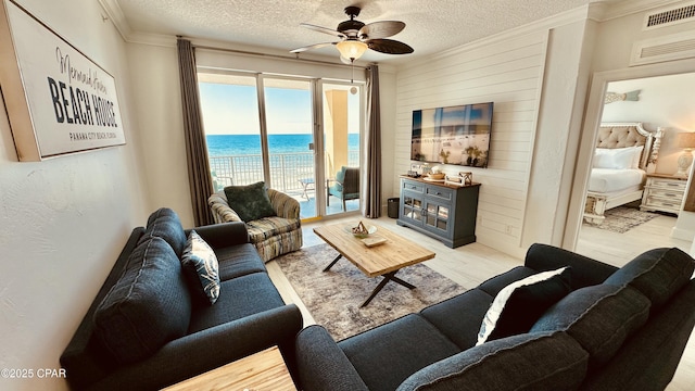 living area featuring ceiling fan, visible vents, light wood finished floors, and a textured ceiling