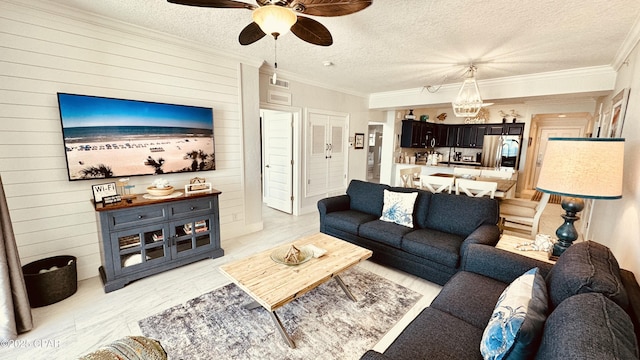 living area with visible vents, ornamental molding, a ceiling fan, a textured ceiling, and wood walls