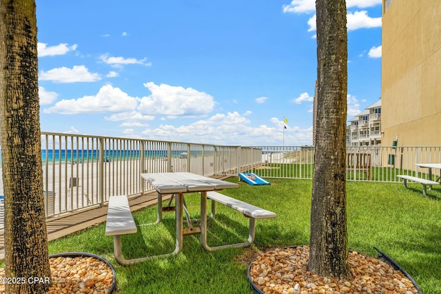 view of yard featuring a view of the beach, a community pool, fence, and a water view