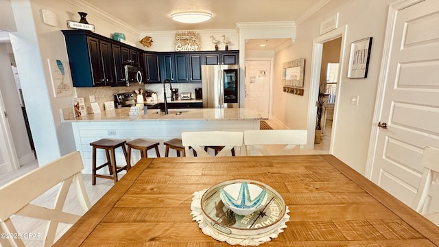 kitchen featuring a peninsula, a sink, decorative backsplash, stainless steel appliances, and crown molding