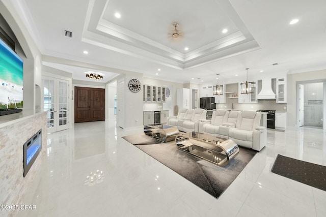 living room with visible vents, a raised ceiling, a fireplace, and crown molding