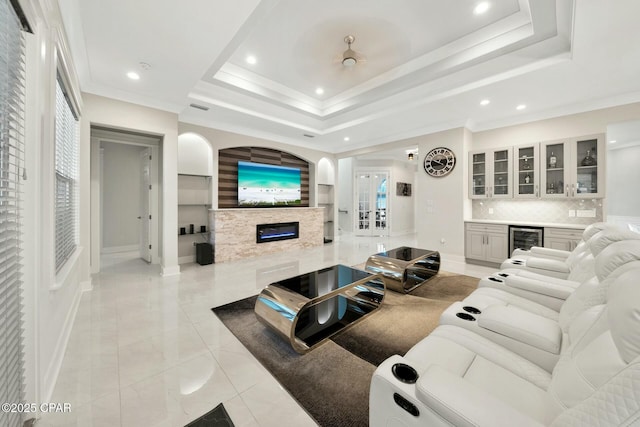 living room with beverage cooler, a tray ceiling, ornamental molding, a premium fireplace, and a bar