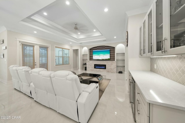 living room with a ceiling fan, a tray ceiling, recessed lighting, a glass covered fireplace, and crown molding