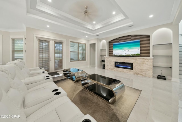 living area with built in features, ornamental molding, a glass covered fireplace, a raised ceiling, and tile patterned floors