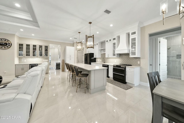 kitchen featuring visible vents, custom exhaust hood, black appliances, a kitchen bar, and a chandelier