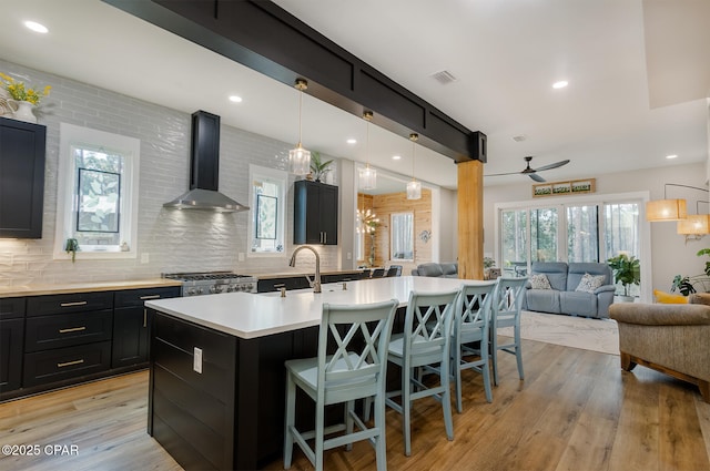 kitchen featuring visible vents, dark cabinets, decorative backsplash, wall chimney exhaust hood, and open floor plan