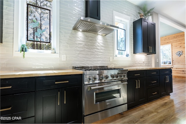 kitchen featuring dark cabinetry, wall chimney range hood, a healthy amount of sunlight, and high end stove