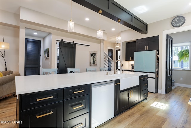 kitchen with dark cabinetry, white appliances, light wood finished floors, a barn door, and beamed ceiling